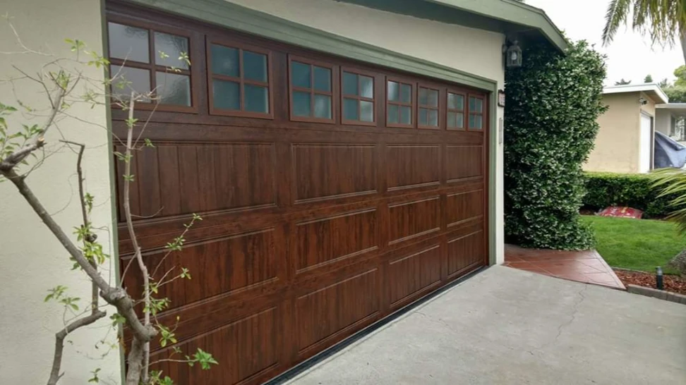 Dark wood-grain finish two-car garage door with a row of multi-pane windows across the top and recessed panels, on a stucco house.