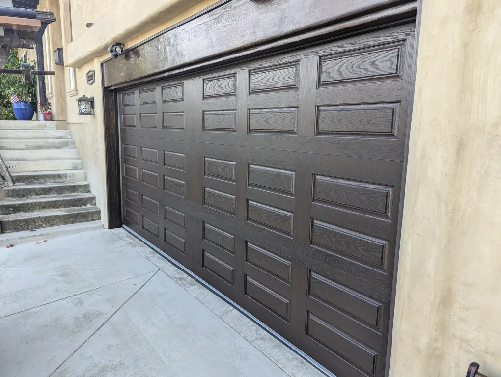 Black farmhouse-style two-car garage door with cross-buck "X" panel design and a row of rectangular windows, on a house with light grey stone veneer.